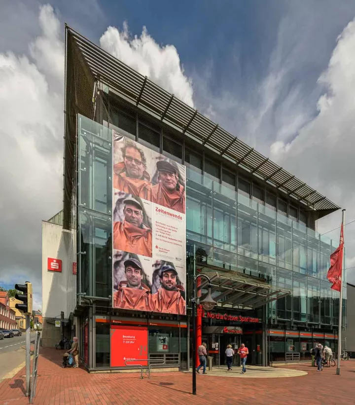 Mit den monumentalen Porträts der fünf Schleifischer vom Holm wirbt ein Außenbanner an der Nord-Ostsee Sparkasse in Schleswig für einen Besuch der Ausstellung "Zeitenwende" (farbige Version).