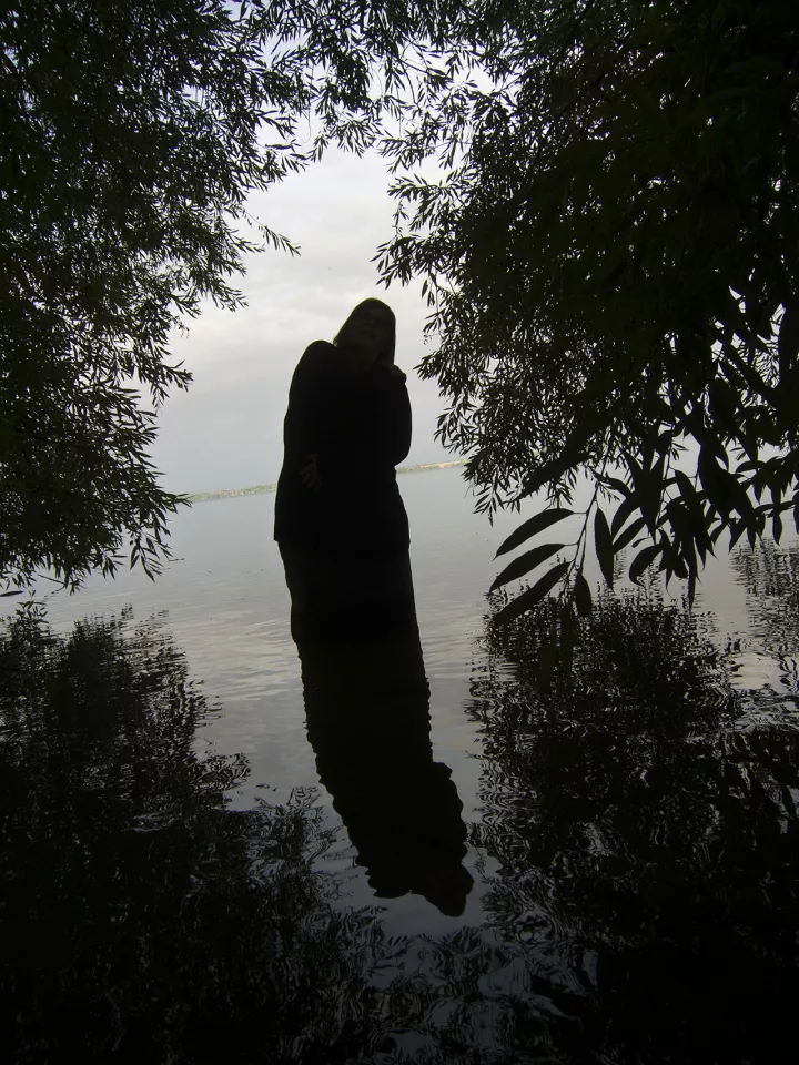 Eine Frau steht im Wasser im Gegenlicht umrangt von Blättern.