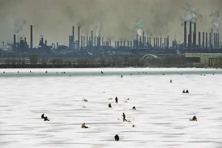 An Winterwochenenden bohren Männer Löcher ins dicke Eis des Ural und versuchen ihr Glück beim Angeln. Da sie wissen, wie stark das Lenin-Stahlwerk im Hintergrund den Fluss verschmutzt, verzehren sie ihren Fang in der Regel nicht selbst, sondern verkaufen ihn auf dem Markt. Magnitogorsk, Russland 1993 © Gerd Ludwig