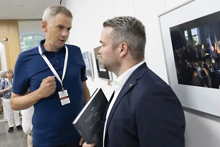 Preisverleihung / Ausstellung "Rückblende 2025" Rainer Schlautmann (DGPh) und Staatssekretär Torsten Wellig, Foto ©Peter Pulkowski - im Hintergrund: Olaf Scholz und Friedrich Merz während der Übergabe des Bundeskanzleramtes an den neuen Bundeskanzler, 6. Mai 2025 © Marco Urban