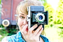 Portrait der Fotografin Jennifer Zumbusch mit analoger Kamera vor der rechten Gesichtshälfte - Instagram