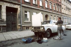 Selbst ist der Mann . . . hat sich wohl auch dieser DDR-Bürger gedacht und seinen Trabi zu Wartungsarbeiten an einem Straßenrand vor Wohnhäusern in Leipzig aufgebockt. (Aufnahme vom 12.3.1989) © picture-alliance / dpa | Wolfgang Weihs